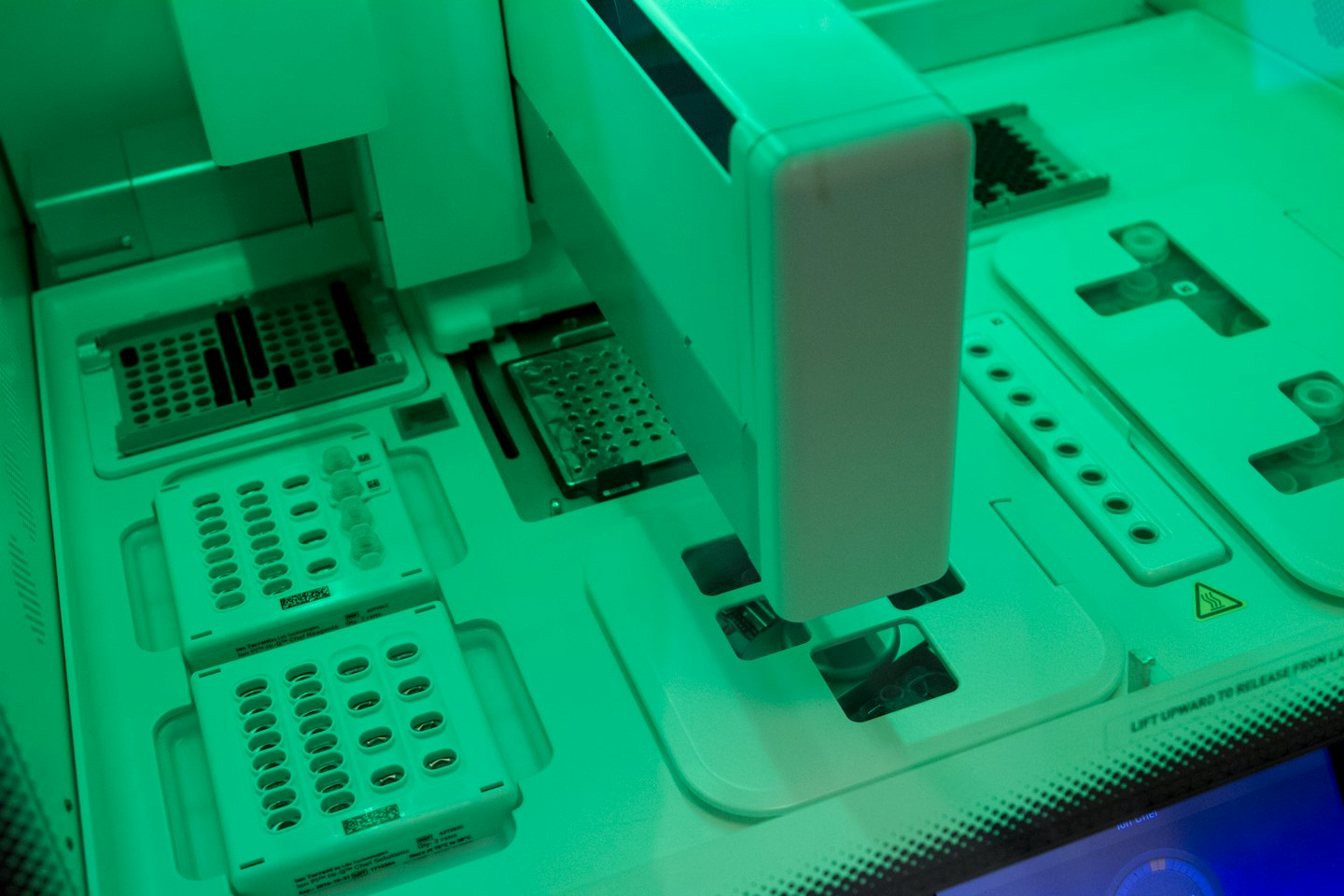 Automated lab equipment with green light illuminating sample trays.